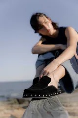 Zuecos de gamuza color marrón chocolate, con base de goma negra, tachas plateadas alrededor de la base y plantilla acolchada.