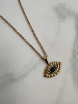 Collar dorado con cadena de eslabones y dije en forma de ojo con piedra azul en el centro.