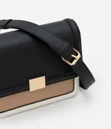 Cartera mediana de PU color negro, con asa transversal regulable, detalle metálico dorado en el frente y recortes contrastantes en beige y blanco.