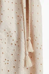Vestido midi color beige con broderie, cuello camisero, botones ocultos, mangas abullonadas al codo, cinturón fino con borlas y ribete festoneado.