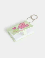 Llavero con dije de libreta de silicona color verde claro, con diseño en relieve de un corazón con la frase "Wake up and do your best", un batido y un corazón pequeño. Incluye cadena metálica con aro.