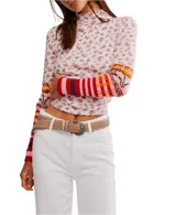 Top de manga larga ajustado, color rosa pálido, con cuello alto y estampado floral diminuto. Las mangas presentan parches de punto con patrones de rayas y cuadros en tonos rojos, naranjas y rosados.