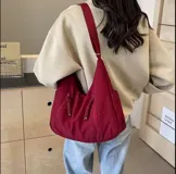 Bolso hobo color bordó de tela suave, liviana y espaciosa, con bolsillos frontales con cierre y correa ajustable.