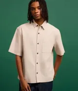 Camisa beige de algodón texturizado, corte boxy, manga corta, cuello inglés y abotonadura frontal.