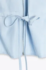 Cuerpo celeste sin mangas, con cuello solapa, escote en pico, bolsillos delanteros con solapa, cintura ajustable con cordón y cierre frontal con cremallera.