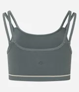 Top deportivo negro, corte tipo bralette, con escote asimétrico y doble tirante en los hombros. Presenta una banda elástica inferior con una delgada línea blanca horizontal.