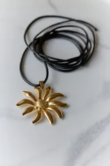 Collar con tiento negro y dije plateado en forma de flor con centro texturizado.