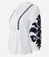 Blusa amplia de viscolino color blanco con bordados florales negros en mangas y escote, lazo en el cuello y mangas 3/4 con puño ajustado.