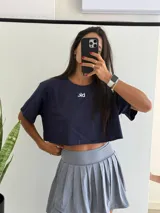 Remera de algodón azul marino, corte crop top y manga corta, con un pequeño logo blanco bordado en el pecho.