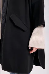 Abrigo negro de paño con corte amplio, cuello camisero, cierre frontal con botones y mangas tres cuartos. Tiene bolsillos laterales y detalle de canesú en la espalda.