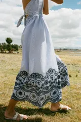 Vestido midi a rayas verticales azules y blancas, con escote en V, tirantes finos y cintura elástica. Presenta bordados florales calados en el ruedo.