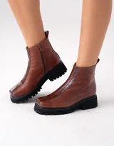 Botas cortas color marrón de cuero vacuno con suela track negra de goma. Presentan cierre lateral con cremallera YKK y puntera cuadrada.