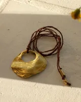 Collar con dije dorado en forma de concha marina y cordón marrón de seda natural.