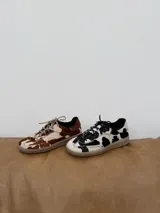 Zapatillas bajas de cuero con estampado de vaca en blanco y marrón.