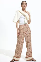 Pantalón de corte holgado en tejido dobby color marrón con estampado de hojas en color crema. Modelo de tiro alto con elástico en la parte posterior de la cintura y cierre oculto con corchete en un lado. Bolsillos laterales discretos y piernas amplias con pliegues adelante y atrás.