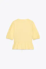 Top amarillo de escote pico y manga corta abullonada con elástico. Detalle de combinación de tejidos a tono y bajo con volante. Cierre frontal con lazadas.