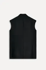 Chaleco negro oversize con cuello solapa de muescas y manga sisa. Tiene falsos bolsillos de vivo en delantero, forro interior a tono y abertura en la espalda. El cierre frontal es cruzado con botones.