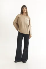 Sweater color beige de tejido de punto, con cuello redondo, manga larga con botón decorativo y bolsillo de parche en el pecho.