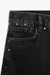Pantalón de jean negro de tiro alto con pierna ancha y detalle de tachas plateadas en los bolsillos y laterales.