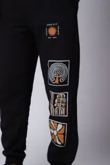 Pantalón de jogging gris claro con puños elásticos, cintura con cordón ajustable y estampado con motivos geométricos en la pierna izquierda.