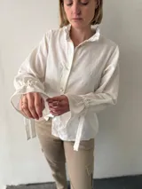 Camisa blanca de tusor de algodón con cuello mao, mangas largas abullonadas con lazo en los puños y botones de nácar. 