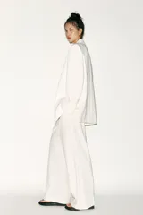 Blazer blanco de corte oversize, con cuello solapa, manga larga con hombreras, bolsillos de doble vivo en el delantero, aberturas en la espalda y cierre cruzado con botones.
