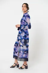 Vestido largo con estampado abstracto en tonos azules, violetas y grises. Tiene cuello mao con abertura en forma de gota, mangas largas acampanadas con detalle de botón en los puños, espalda abierta, tajo frontal y flecos en el ruedo.