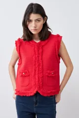 Chaleco tejido color rojo con cuello redondo, sin mangas, con desflecado en bordes y bolsillos frontales con botones dorados.