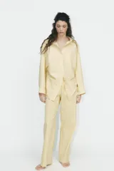 Camisa oversize a rayas amarillas y blancas, de cuello solapa y manga larga tipo murciélago acabada en puño con hombro caído. Tiene un bolsillo de plastrón en el delantero y cierre frontal con botones.