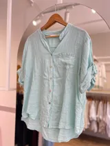 Camisa celeste de lino, con cuello mao, manga 3/4 con botón para sujetar, cierre frontal con botones y bolsillo de parche en el pecho.