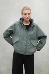 Campera color crema de corte oversize con capucha ajustable, cierre frontal con botones a presión y bolsillos laterales con solapa. Fabricada con poliamida reciclada, impermeable y transpirable.