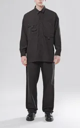 Camisa negra de manga larga, estilo técnica con múltiples bolsillos delanteros y un bolsillo en la parte inferior de la espalda, botones en cartera y mangas, calce oversize, confeccionada en textil ligero suave al tacto.