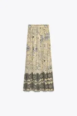 Falda larga color crema con estampado floral en tonos negro y dorado, cintura elástica con cordón ajustable y borlas decorativas.