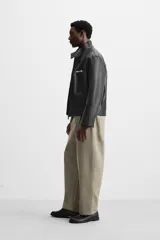 Pantalón negro de corte amplio tipo balloon fit, con cintura con pliegues frontales, bolsillos delanteros y traseros de plastrón. Cierre frontal con cremallera y botón.