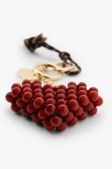 Llavero con cordón marrón y blanco, llave dorada y dije colgante de corazón rojo hecho con cuentas. Incluye aros metálicos dorados.