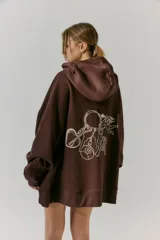 Buzo marrón de frisa con capucha y bolsillos delanteros. Corte oversize, recortes laterales y doble cordón con puntera de goma. Estampa en frente y espalda realizada en serigrafía con diseño de llavero con dijes.