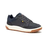 Zapatillas urbanas CAT modelo Apa Cush, color azul marino con detalles en naranja y suela de goma color caramelo. Capellada de cuero recubierta con PU, forro de malla interior hecho con residuos industriales 100% reciclados, plantilla acolchada de espuma, entresuela de EVA duradera y liviana y construcción Strobel.