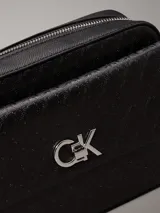 Bandolera negra con monograma CK grabado en toda la superficie. Tiene correa de cadena plateada, cierre superior con cremallera, bolsillo frontal con cierre giratorio y herrajes plateados.