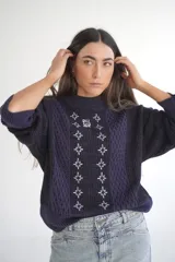 Sweater de punto azul marino con cuello redondo y mangas largas. Presenta textura trenzada en los laterales y detalle de estrellas bordadas en blanco en el centro, con la inscripción "Del Sur" en la parte superior.