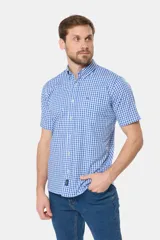 Camisa de manga corta con estampado a cuadros azules y blancos, bolsillo en el pecho con logo bordado y botones personalizados. Hecha en Uruguay.