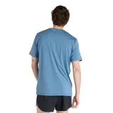 Remera celeste de hombre, marca New Balance, modelo Performance. Tiene mangas cortas y logo estampado en el pecho con diseño multicolor.
