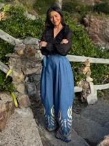 Pantalón de jeans azul con corte palazzo, cintura alta con lazo y bordado decorativo en el ruedo.