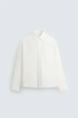 Camisa de manga larga color blanco hueso, de corte recto y cuello italiano. Tiene un bolsillo de parche en el pecho y cierre frontal con botones.
