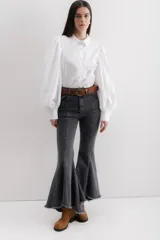 Pantalón de jean negro elastizado con corte ajustado y volados en la parte baja de la pierna. El ruedo es más largo en la parte trasera y tiene terminación descosida.