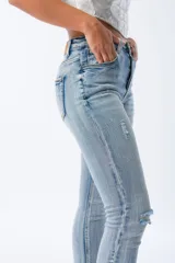 Pantalón de jean celeste claro, corte skinny, con roturas en las rodillas y muslos, tiro alto y cierre con botones.