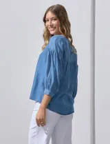 Blusa celeste de lyocell con cuello a la base y escote en V con apertura central y botones. Manga ¾ con puño y botón.