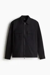 Sobrecamisa negra de algodón con cuello inglés, cierre bidireccional, bolsillos superiores con solapa y botones a presión, canesú en la espalda, bajo recto con aberturas laterales y mangas largas con tapeta de manga y botón a presión en los puños.