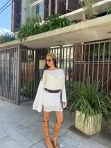 Vestido corto blanco traslúcido con mangas largas acampanadas, cinturón ancho marrón con flecos y sombrero de paja.