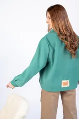 Chaqueta verde con apliques dorados en los bolsillos y cierre frontal con botones.