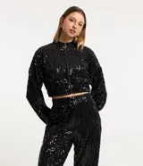 Campera bomber corta negra cubierta de lentejuelas metalizadas, con cuello alto, mangas largas, puños y bajo elásticos, y cierre frontal con cremallera.